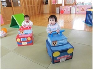 車の乗り物に乗って室内で遊ぶ乳幼児2人