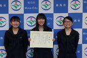 三人の女子高校生がカメラに笑顔を向けている写真。真ん中の女の子が賞状を持っている。