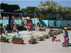 土の園庭で園児たちが奥のブランコや手前で三輪車に乗っている様子の画像