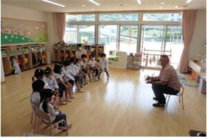 教室で椅子に座って先生から英語を教わる園児たちの様子