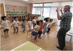 椅子から立ち上がり、先生の問いかけに体を動かして応える園児たちの様子