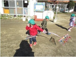 園庭で手作りの凧をあげて遊ぶ園児たちの様子