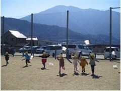 園庭で凧揚げをする子どもたちの奥に山が見える様子