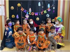 ハロウィンの飾りつけの中で保育士とかぼちゃの仮装をした子どもたちの記念写真