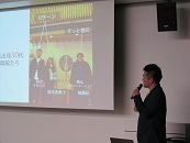 講師の木藤亮太氏が、前に立ってマイクを持ち、スライドを見ながら話をしている写真。