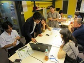研修の参加者たちが、グループに分かれてパソコンを見ながら、話し合いをしている写真。