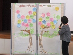 美馬市の未来のために自分ができることを書いた花びら型の色紙で飾った大きな木の台紙と内容を読み上げる人の画像